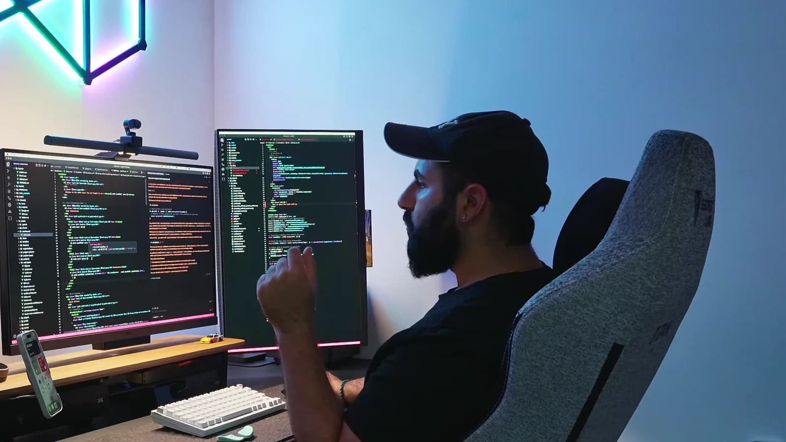 Peter writing code at his desk, two monitors full of code